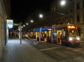 Straßenbahn direkt vor der Kreuzung in Haltestelle mit befahrbarem Kap, Fahrgäste queren dieses um zuzusteigen
