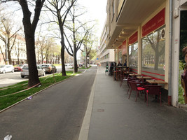 Asphaltierter Radweg und asphaltierter Gehsteig eingeengt durch Schanigarten, links daneben eine Grünfläche und wiederum daneben eine KFZ-Fahrspur