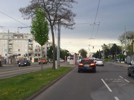 Starße mit mehreren Fahrspuren in Blickrichtung, rechts am Fahrbahnrand eine Bushaltestelle, links ein eigener Gleiskörper mit Haltestelle ein Fahrtrichtung der Blickrichtung, weiter links Fahrbahn der Gegenrichtung mit Bushaltestelle