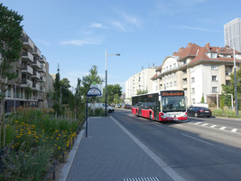 Breite Straße mit mehreren Fahrspuren, auf einer kommt ein 22A-Bus, daneben eine Haltestelle, daneben großzügige Grünflächen